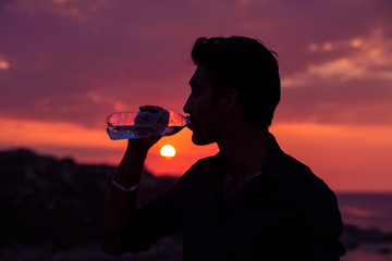 Profile of man silhouette drinking water from a bottle at sunset