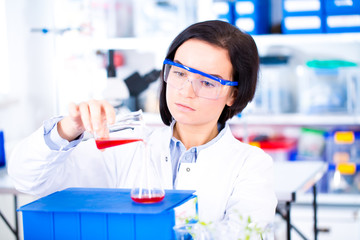 Attractive young female scientist working in laboratory.  Woman scientist looking at a red test tube in a lab