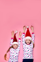 Two sisters lying on the floor on a pink background in pajamas 