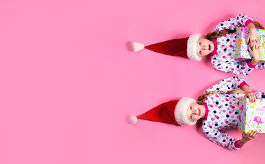 Two sisters lying on the floor on a pink background in pajamas 