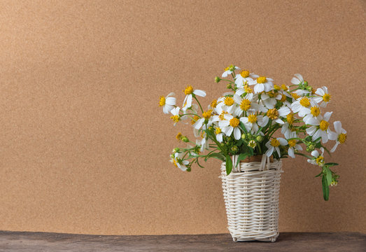 white flowers in basket on wooden table with brown paper background