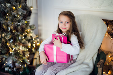Fototapeta na wymiar Beautiful girl near Christmas tree unpacking presents sitting on a chair