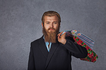 sale, consumerism concept - serious young  bearded business man with shopping bags grey background