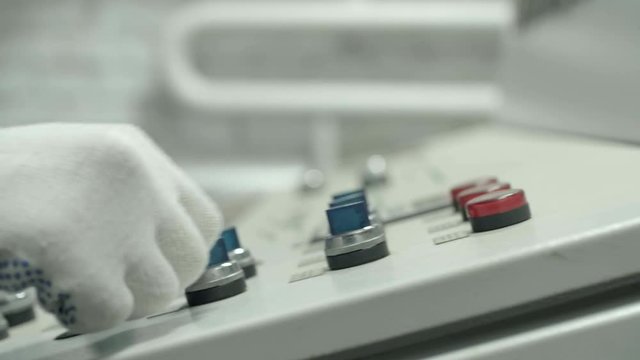 A machine operator hand turns on at control panel of industrial machine. A slight movement of camera