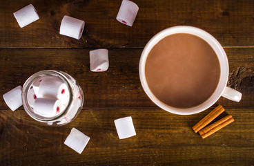 cup of cocoa with marshmallows and a bank on a wooden background