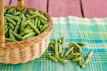 Unopened pea pods in a basket on wooden background.