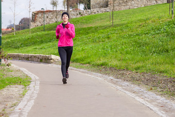 Young woman running on a cold winter day on an urban park.