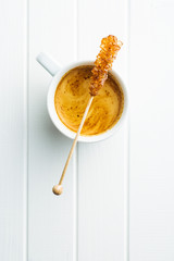 Brown amber sugar crystal on wooden stick and coffee cup.