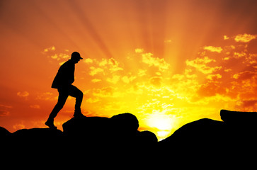 Silhouette of a man climbing on top of a mountain againt sunrise