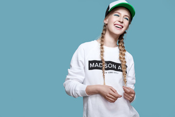 Laughing girl in a baseball cap and a white hoodie is on a blue background