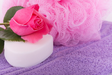 Obraz na płótnie Canvas Soap with a pink rose on top of a purple towel, with a pink shower puff on background