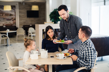 Waiter serving family in a restaurant and bringing full plate