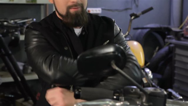 Bearded male biker crossing his arms on his chest on the motorcycle. Close up of attractive caucasian man touching the handle of motorcycle accelerator. Cool man in black leather jacket sittting on