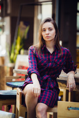 Above view pretty woman in violet checkered dress sitting at table on terrace in cafeteria. She looking to camera