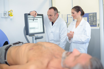 Obraz premium Man undressed on hospital bed, medics looking at computer