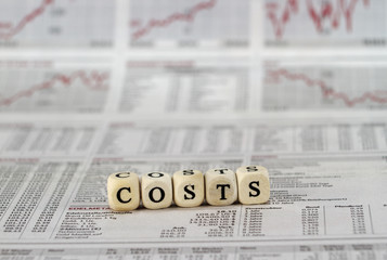costs word built with letter cubes on newspaper background