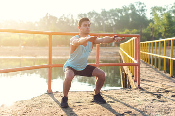 Fit man warming up doing squats stretching arms forward outdoors.