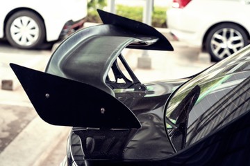car part ; Close up detail of a custom racing carbon fiber spoiler on the rear of a modern car with...