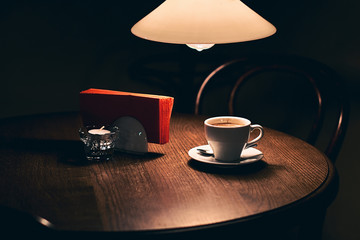 Cup of coffee on a vintage wooden cafe table under an old lamp in a dark interior