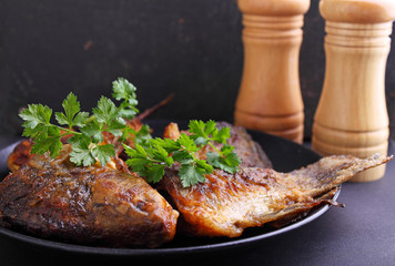 Fried fish on a black plate decorated with fresh parsley on a black background