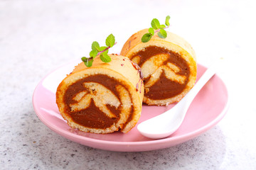 Swiss roll with condensed milk in a pink plate decorated with mint