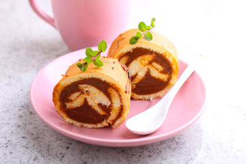 Swiss roll with condensed milk in a pink plate decorated with mint