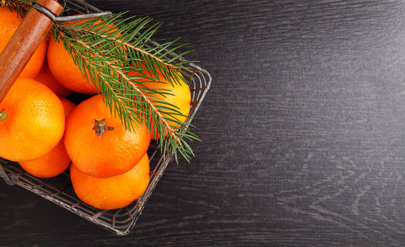 Tangerine in a metal basket with a branch of a Christmas tree on a black background