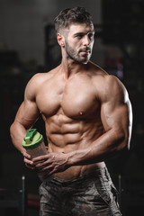 Fototapeta na wymiar Handsome athletic fitness man holding a shaker and posing gym