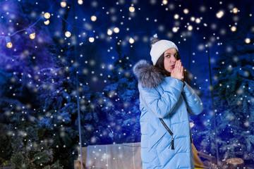 Young woman in blue down jacket warming hands and standing near