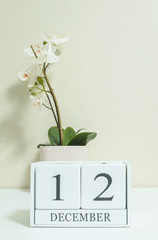 Closeup white wooden calendar with black 12 december word with white orchid flower on white wood desk and cream color wallpaper in room textured background , selective focus at the calendar
