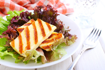 green salad with fried halloumi cheese in a white plate on a white wooden background