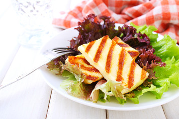 green salad with fried halloumi cheese in a white plate on a white wooden background