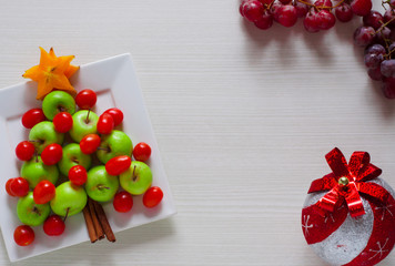 design decor serving of fruit themed Christmas tree made of green apple, cherry tomatoes and red grapes with white wood background