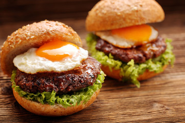 Hamburger with beef meat and fried egg on wooden background