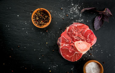 Fresh raw beef meat on a black slate stone background. With spices for cooking, copy space, top view