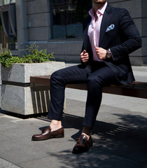 Male model in a suit sitting on a bech outdoors