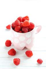 Red raspberries in mug on a white wooden table