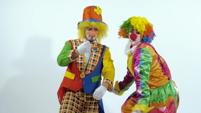 Two amusing clowns dancing together, when one of them drops the glasses