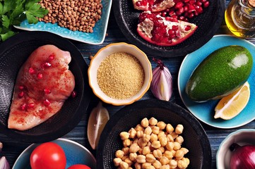 Ingredients of middle eastern cuisine - chickpeas, lentils, couscous, pomegranate, red onion, tomato, avocado, chicken breast, paprika, parsley, olive oil and garlic.