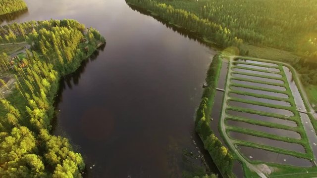 Backwards aerial overflight shot of rapids and fish farm pools at a Nordic river