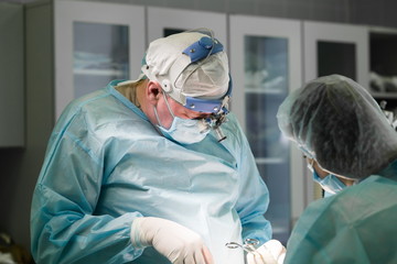 Surgeon performing cosmetic surgery in hospital operating room. Surgical team at work. Breast...