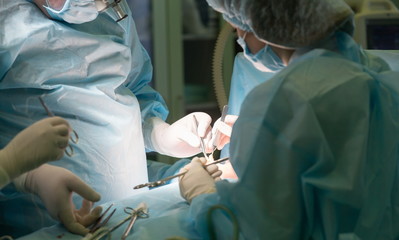 Surgeon and his assistant working on a patient during cosmetic surgery in hospital operating room. Surgeon holding surgical instrument during medical procedure. Plastic surgery, breast augmentation.