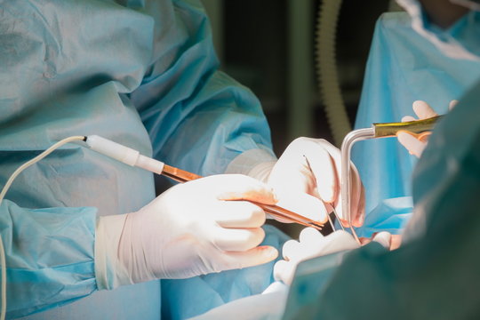 Close-up shot of surgeon and his assistant performing cosmetic surgery in hospital operating room. Doctor holding surgical instruments during medical procedure at clinic. Breast augmentation.
