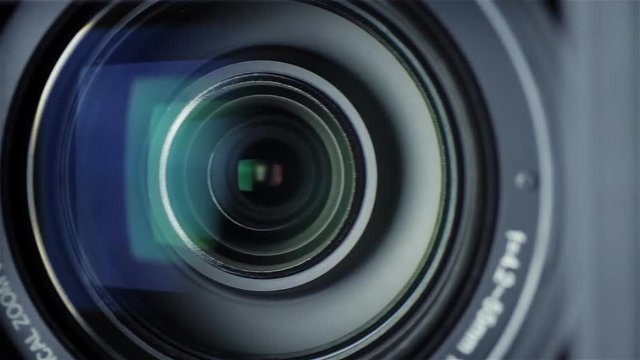 Closeup shot of a professional video camera while it's lens is zooming. The camera is turning towards the audience.
