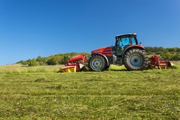 Agricultural work. Red tractor mowing the meadow, Czech Republic. Farmer harvested hay.
