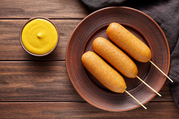 Corn dog traditional American corndog street junk food deep fried hotdog sausage with mustard snack treat coated in a thick layer of cornmeal batter on stick unhealthy eating on rustic wooden table.