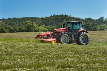 Obraz premium Agricultural work. Red tractor mowing the meadow, Czech Republic. Farmer harvested hay. 