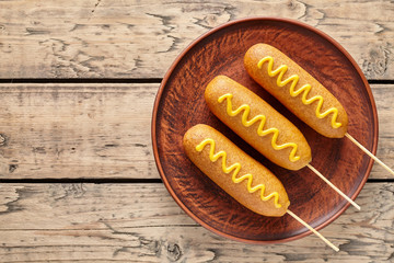 Corn dog traditional American junk food fried hotdog meat sausage snack with mustard snack treat coated in a thick layer of cornmeal batter on stick unhealthy eating on rustic wooden table.