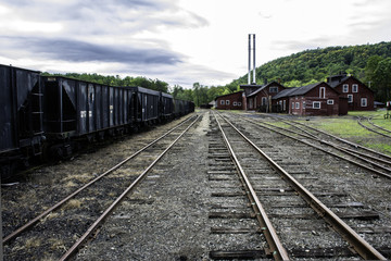 Fototapeta na wymiar tracks running through old railroad yard next to rusting coal hoppers and maintenance shops
