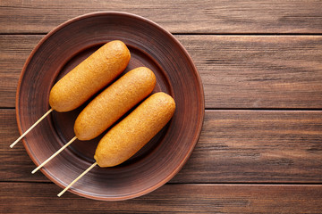 Corn dog traditional American street junk deep fried hot meat sausage snack treat coated in a layer of cornmeal batter on stick on wooden rustic table.